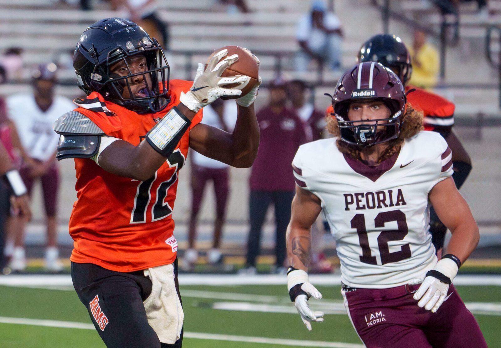 Manual’s Kieyer Wells, left, catches a pass with Peoria High’s Jacob Merna in pursuit in the first half of their Week 4 high school football game Friday, Sept. 11, 2026 at Peoria Stadium. The Lions blanked the Rams 50-0.